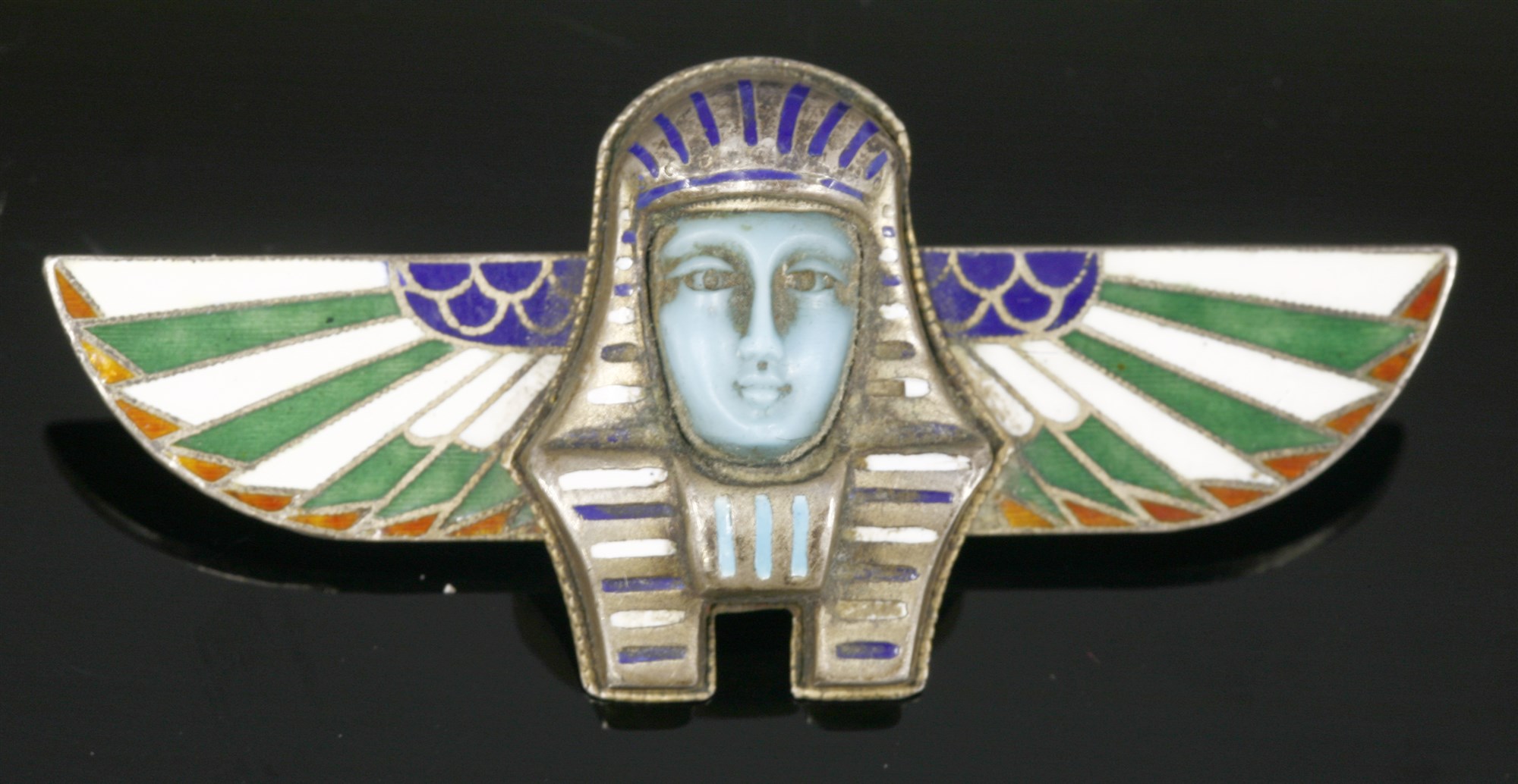 An Egyptian Revival silver and champlevé enamel brooch, in the form of a ba-bird. The ba is an aspect of a person’s non-physical being, or ‘soul’, and could travel out of the tomb after death. The ba was usually represented as a bird with the head of a human, and sometimes with human arms. Silver gilt enamelled pieces of this sort are typical of the Art Deco Egyptian Revival, usually Continental in make (either French or German), and often set with marcasite.  Lot 10, 20th Century Decorative Art & Design Sale, 13th October 2015 Hammer £75